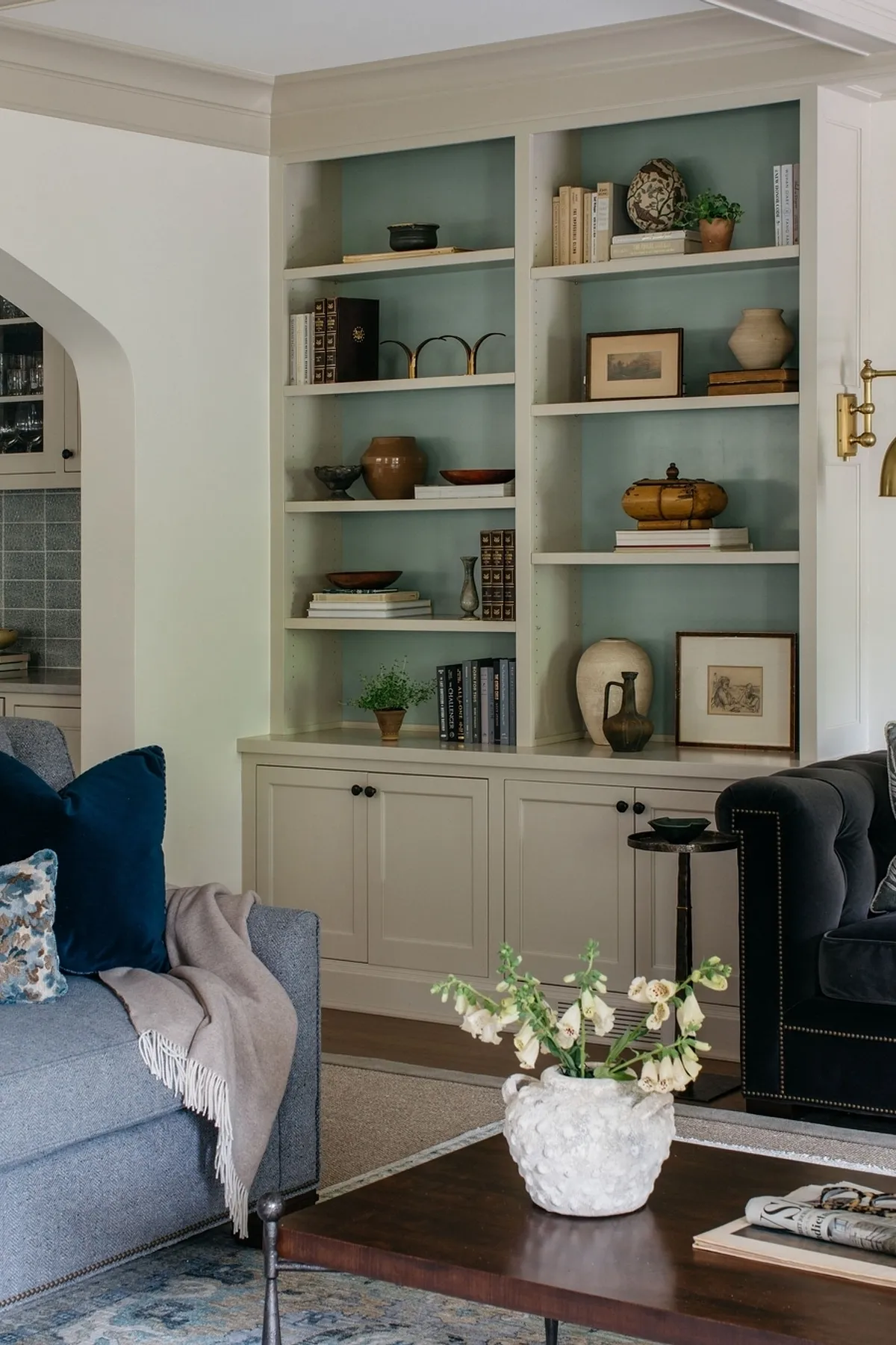Stylish living room shelf with green backdrop, ceramic decor, framed art, and layered books.