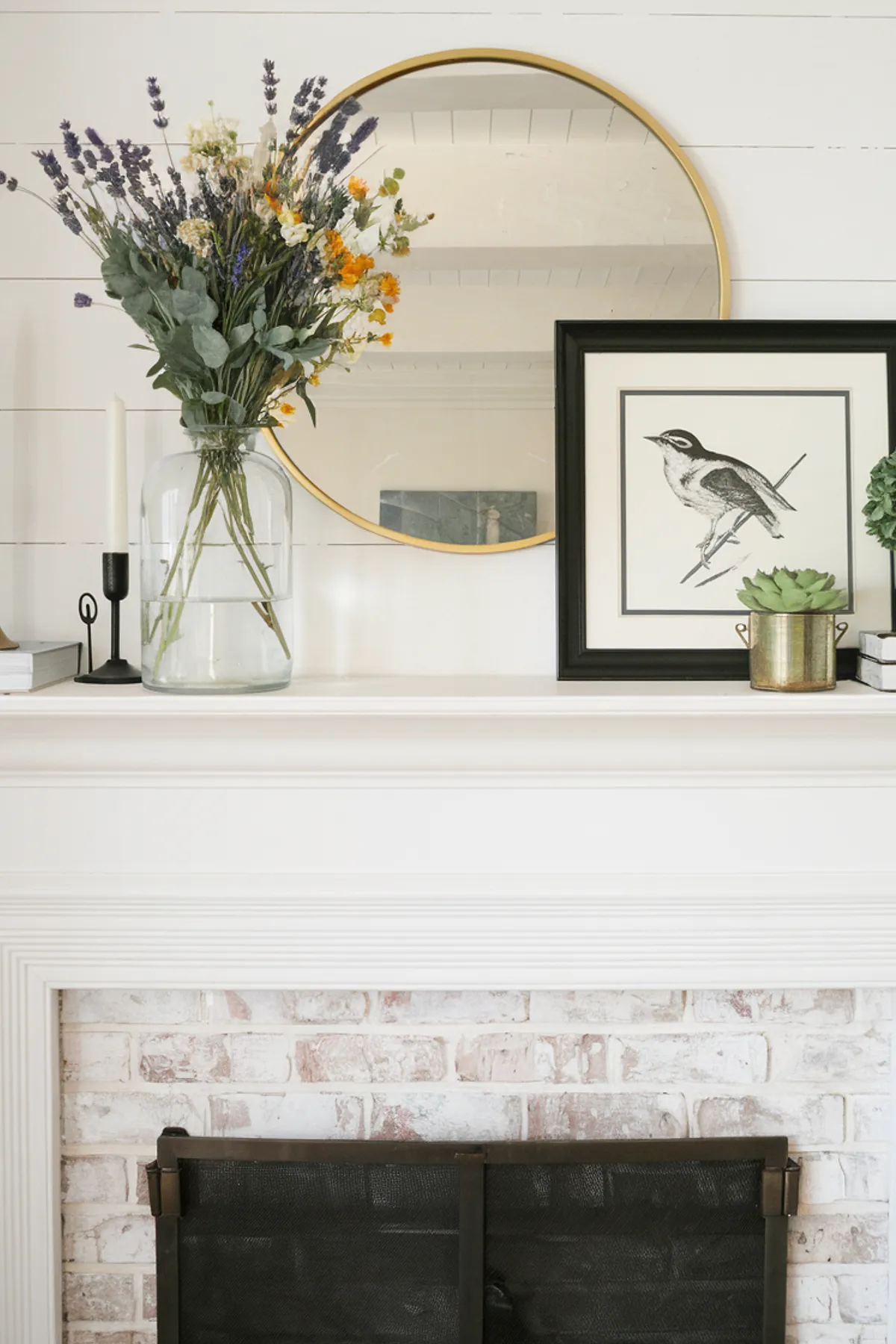 A spring mantel featuring wildflowers in a vase, a mirror, and framed artwork.