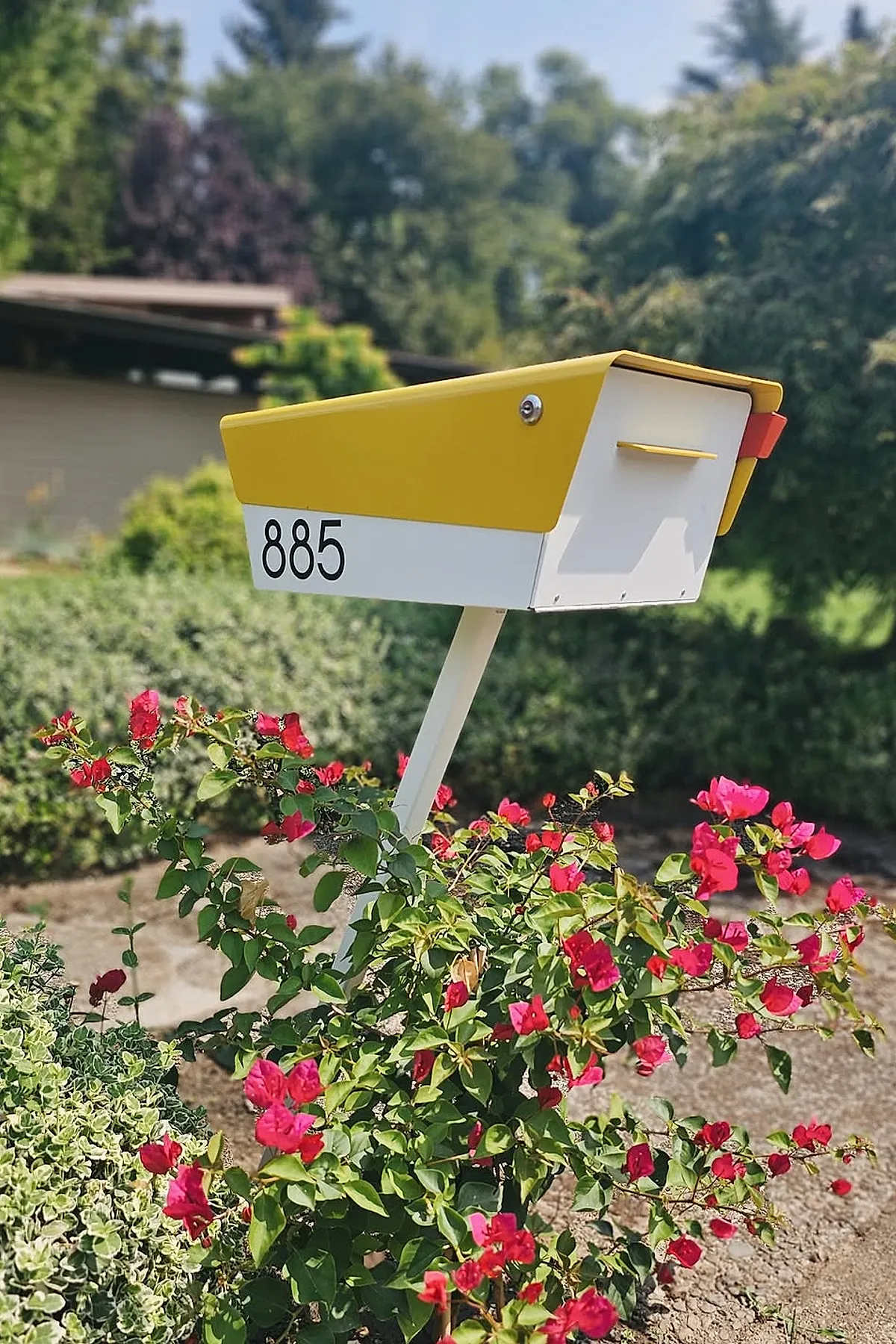 A modern mailbox painted yellow on top and white on the bottom with black house numbers