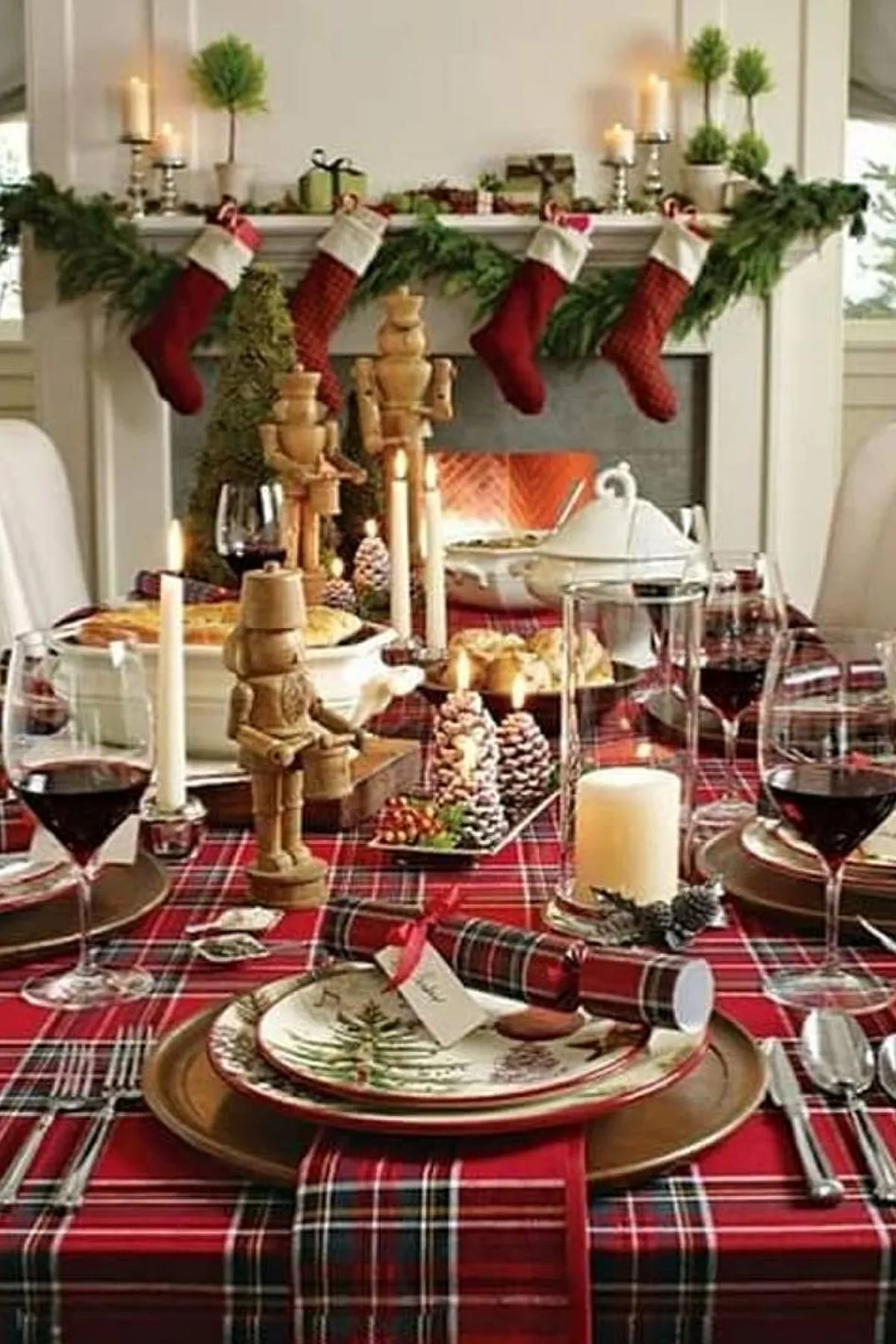Festive Christmas table with plaid tablecloth, nutcracker centerpiece, red wine glasses, and a cozy fireplace view.