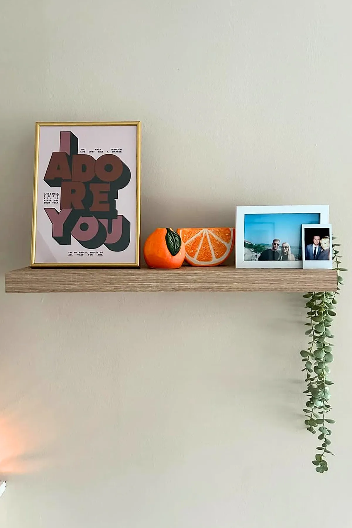 Minimalist wall decor featuring a floating wooden shelf with a gold-framed artwork saying