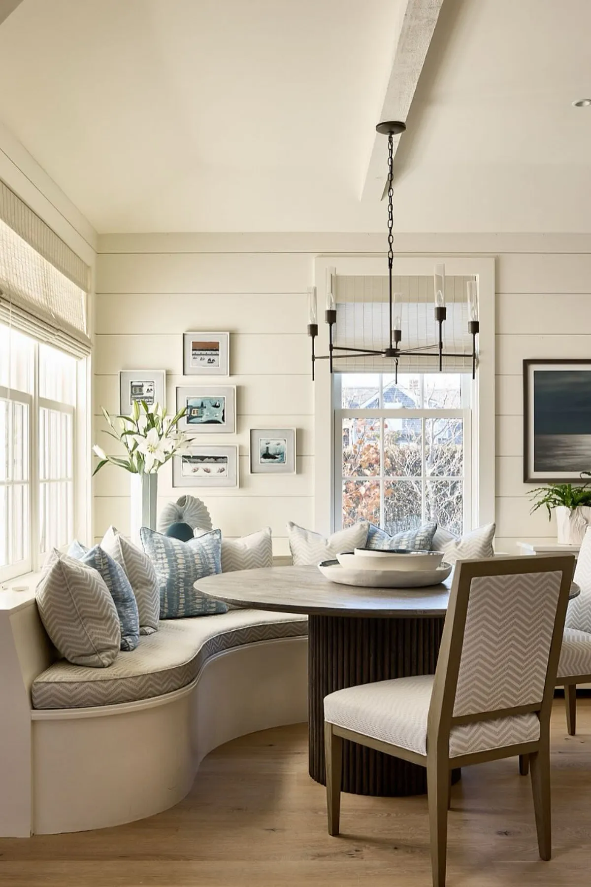 Modern breakfast nook featuring curved seating, blue accent pillows, round table, and natural light.