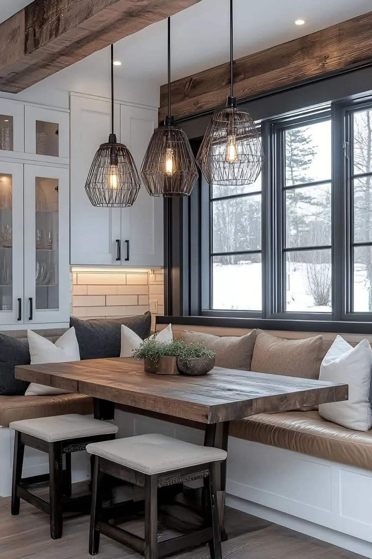 Cozy breakfast nook featuring a wooden table, cushioned bench seating, industrial light fixtures, and large windows.