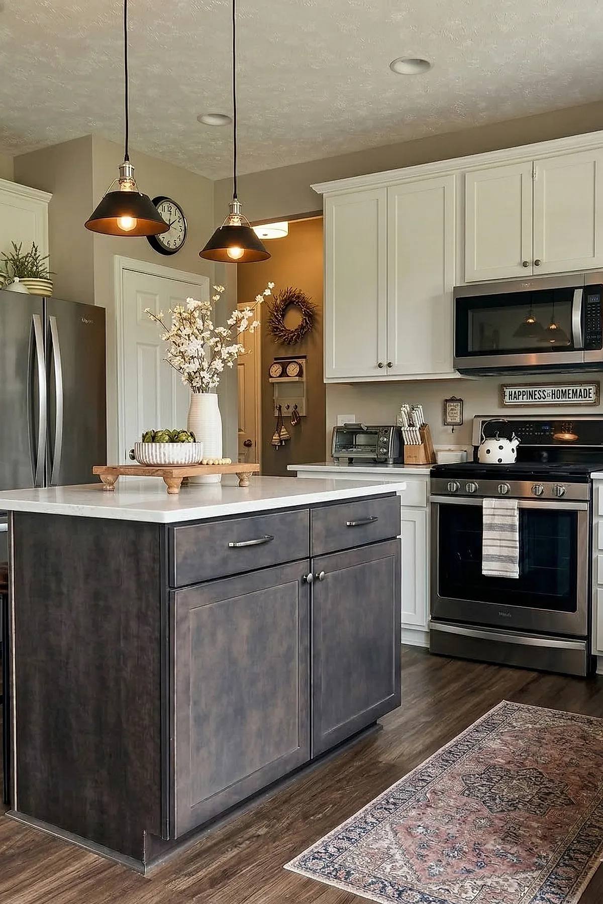 Modern kitchen with dark wood kitchen island topped with white countertop, decorated with a white vase holding white flowers and a striped ceramic bowl filled with artichokes, illuminated by two black pendant lights above.