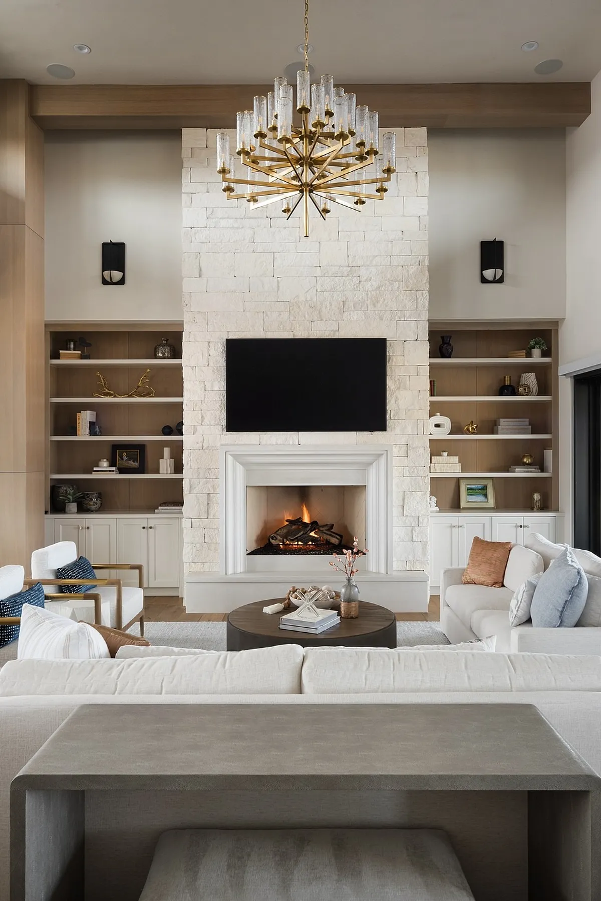 Elegant living room featuring a white stone fireplace, modern TV wall, stylish shelves, and cozy seating arrangement.
