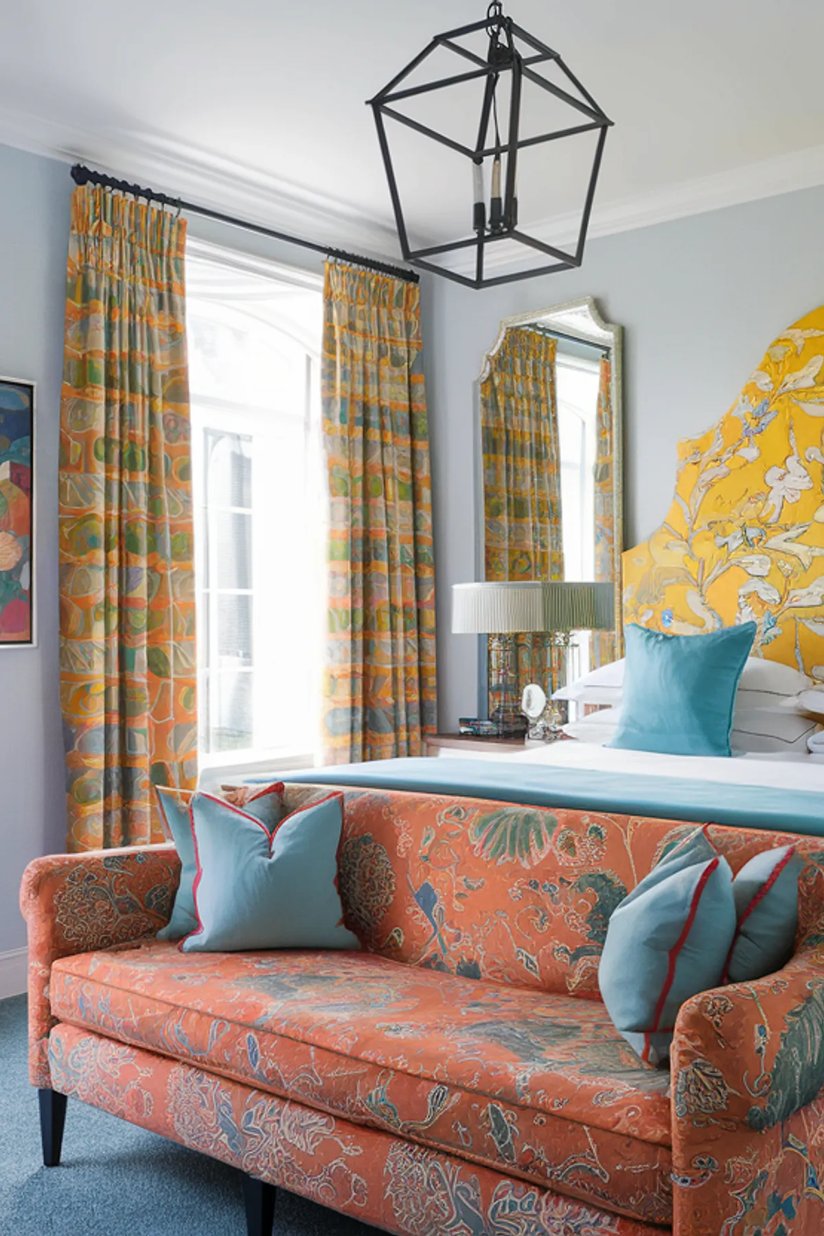 Vibrant bedroom with yellow floral headboard, rich orange sofa, and light blue walls.