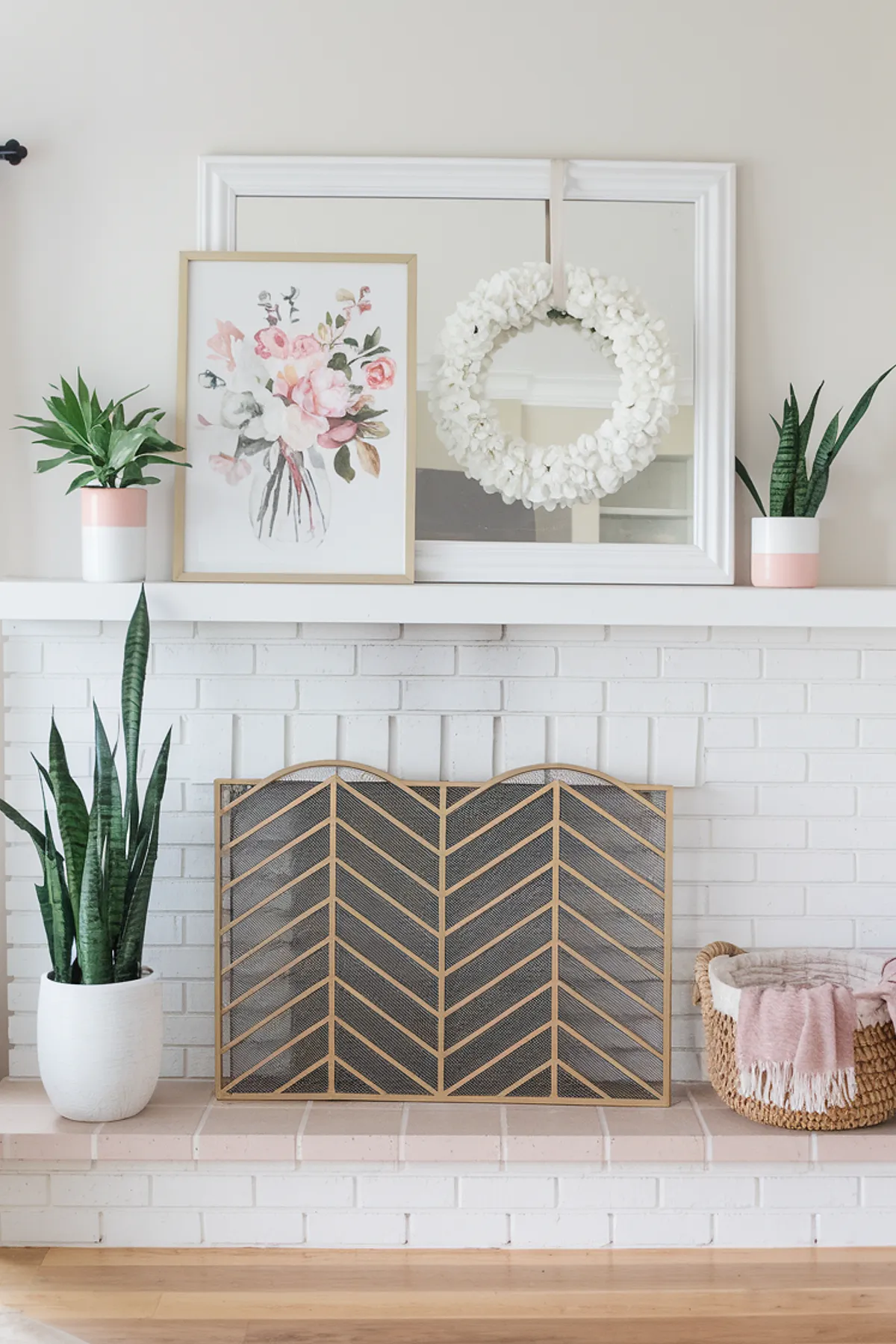 A spring mantel featuring floral artwork, a white wreath, and potted plants.