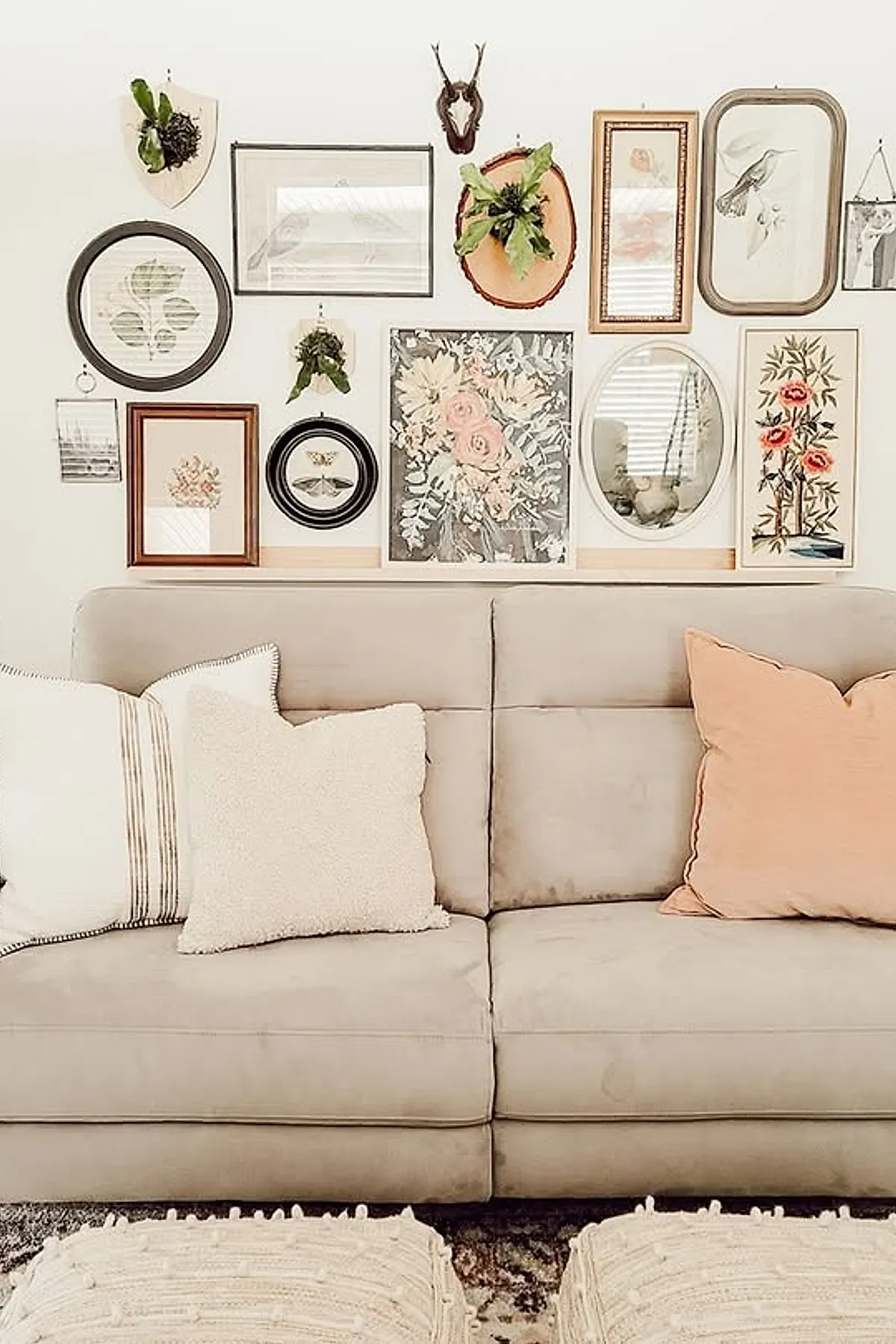 Neutral-toned living room wall decor featuring an eclectic gallery wall of framed botanical prints, sketches, and mounted greenery above a beige sofa with cream and peach throw pillows and textured cream ottomans in front.