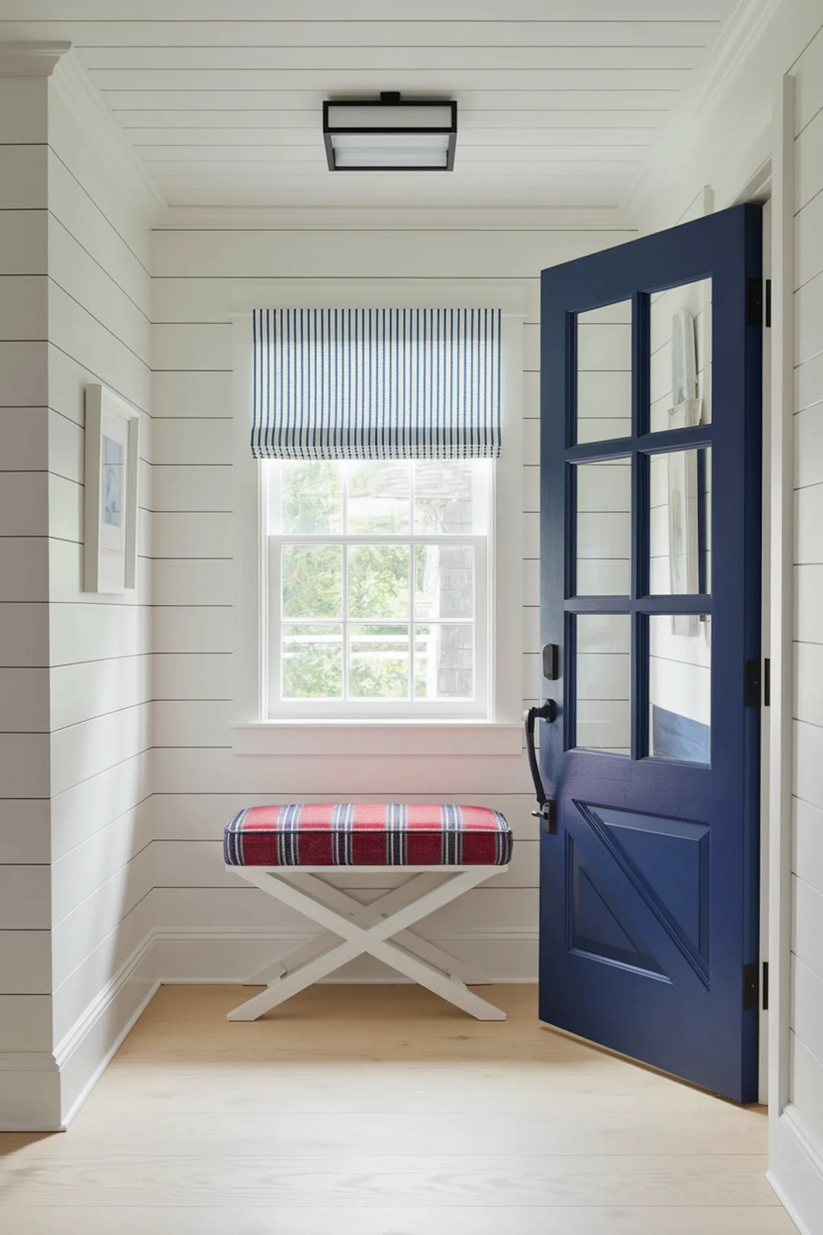 A coastal entryway with a navy blue door and a blue and red striped bench and blue and white striped window treatment