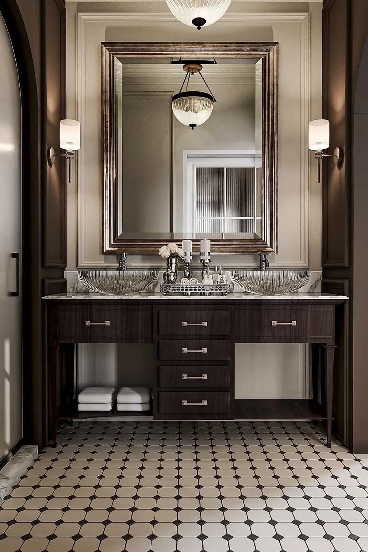 Luxury master bathroom with a dark wood vanity featuring multiple drawers, two clear ribbed glass vessel sinks, large framed mirror above, marble countertop, wall sconces on either side of the mirror, and patterned black and white tile flooring.