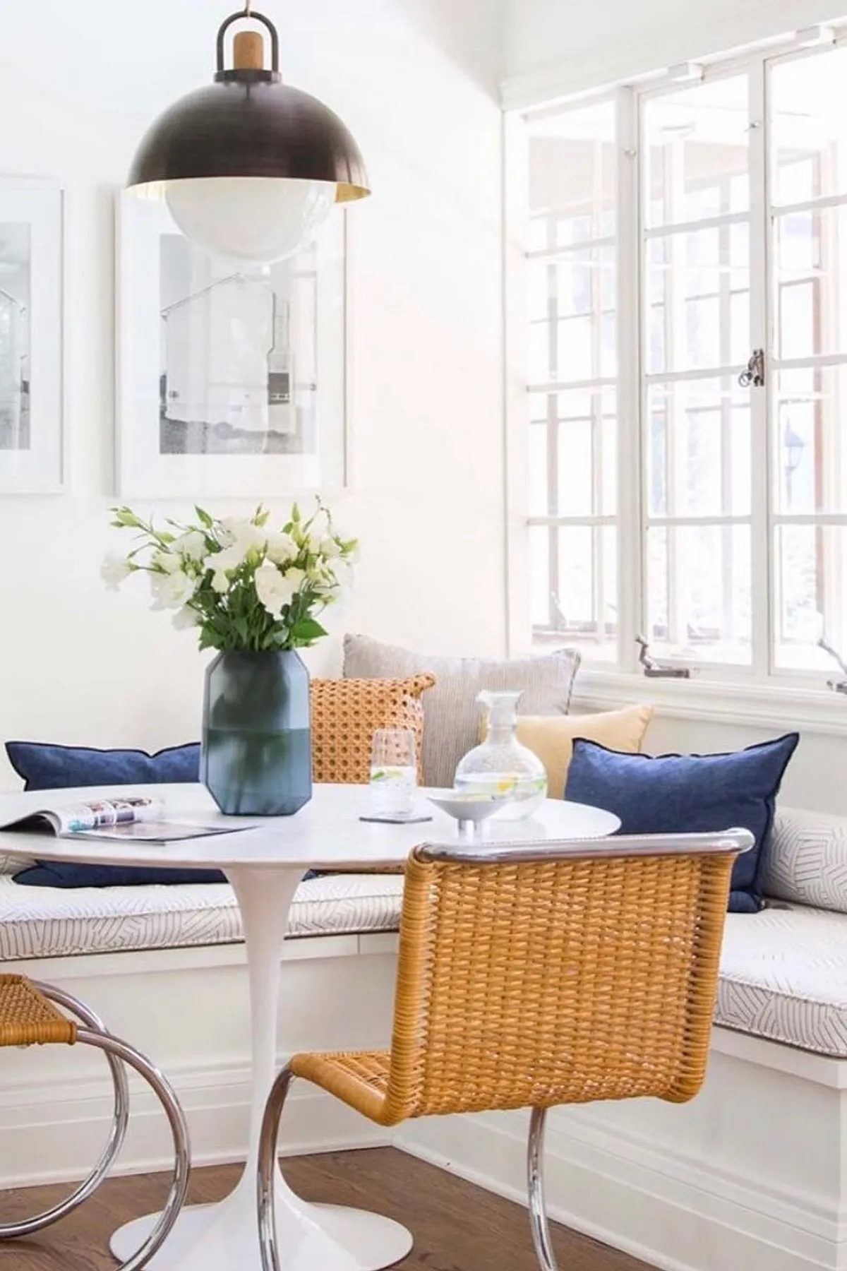 Bright breakfast nook featuring a white table, wicker chairs, floral arrangement, and large windows.