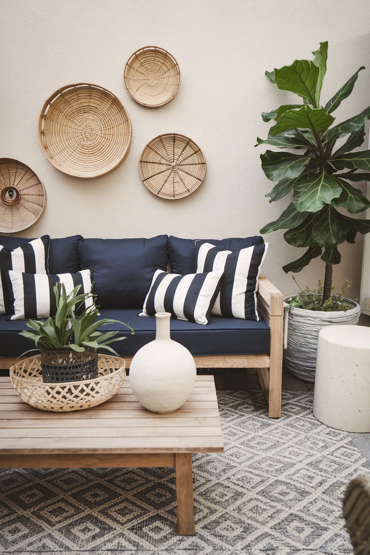 A chic patio featuring a navy couch, striped pillows, woven baskets on the wall, and a leafy plant.
