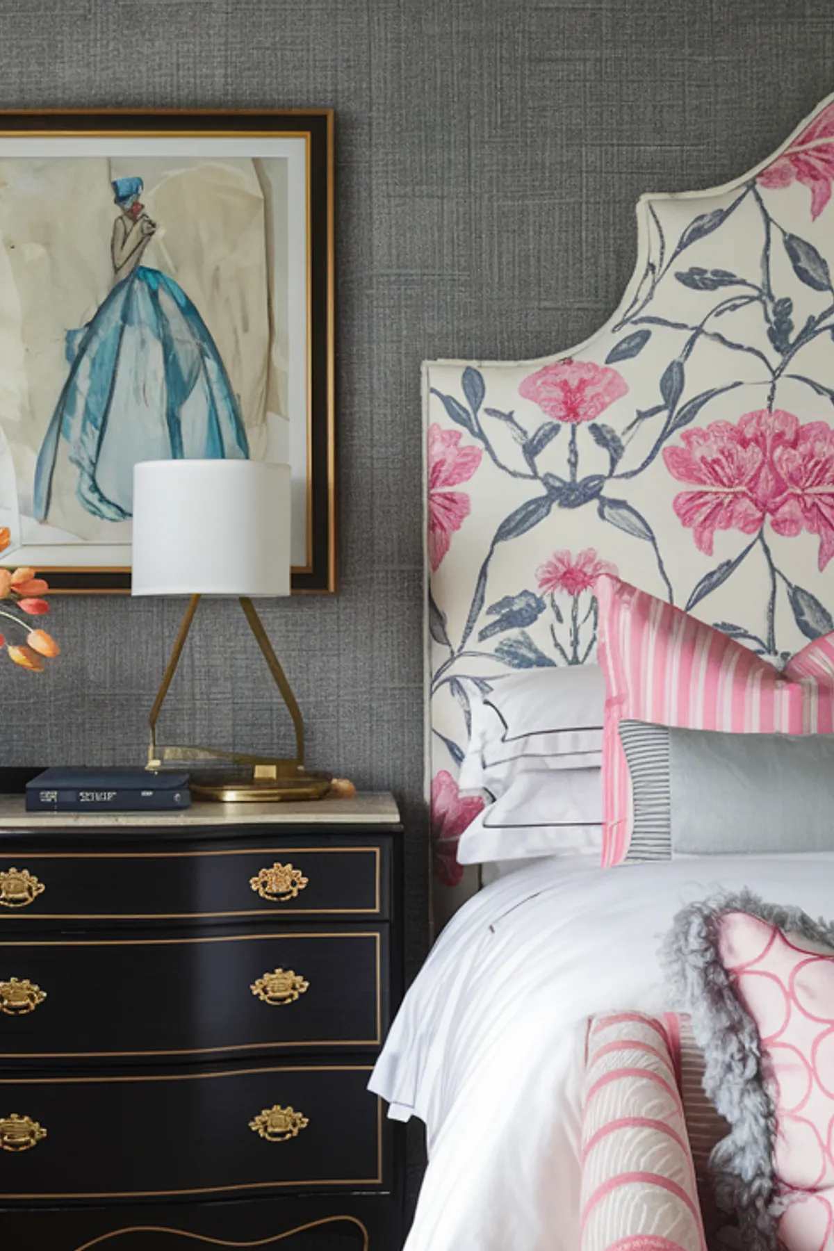 Bedroom with floral headboard, black chest with gold accents, and pink geometric armchair.