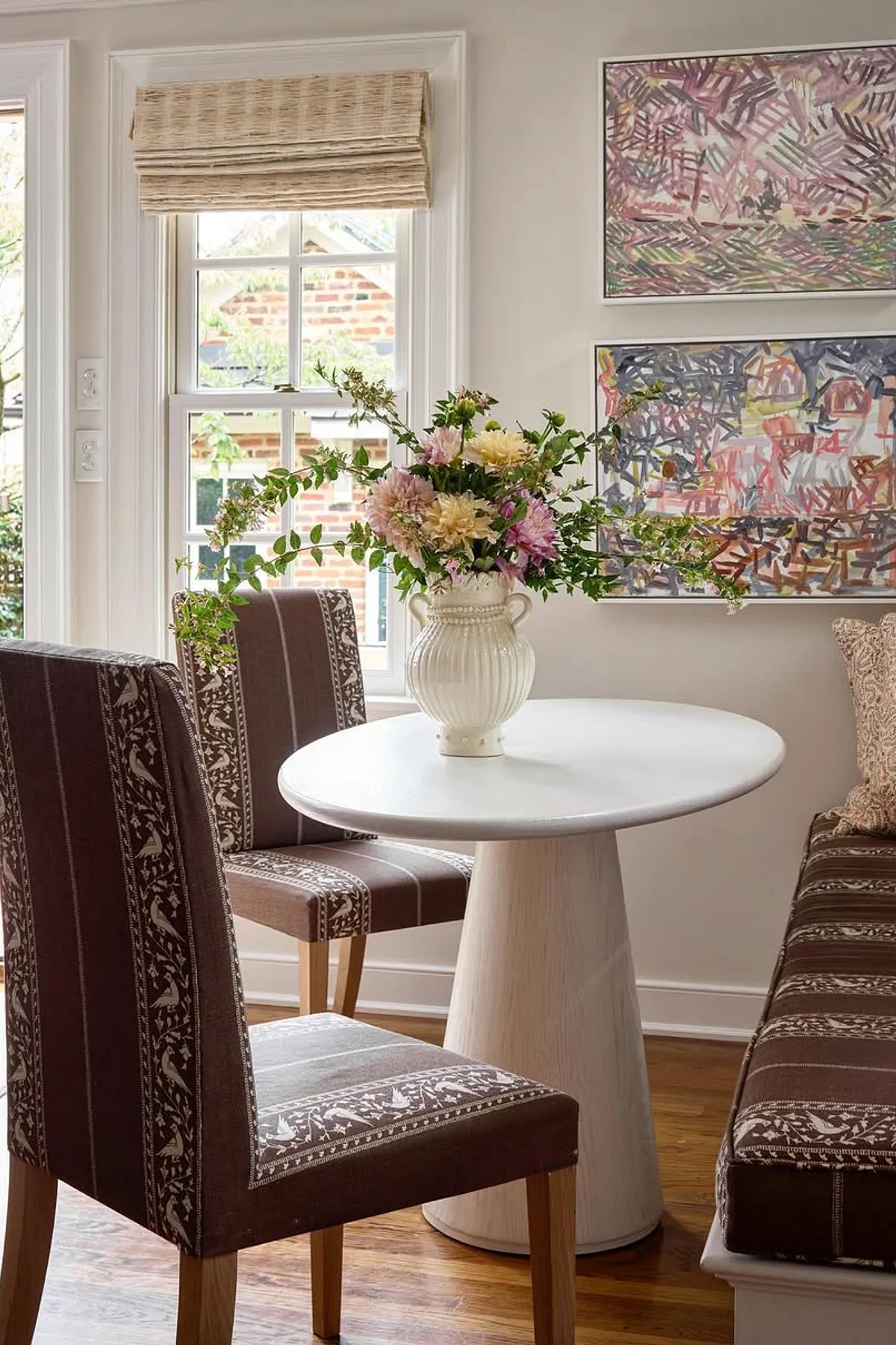 Charming breakfast nook featuring a round white marble table, brown patterned chairs, and a floral arrangement.
