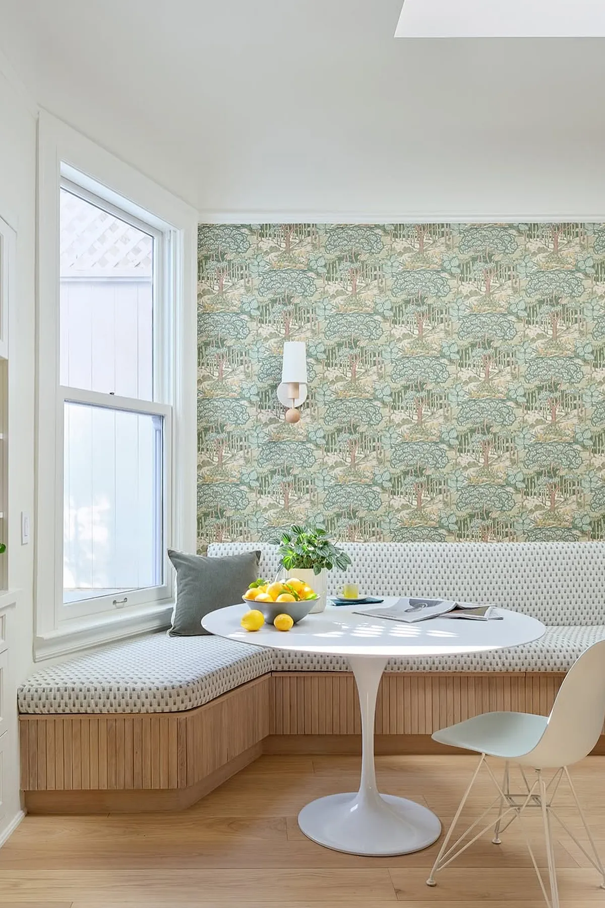 Charming breakfast nook with floral wallpaper, white round table, cozy bench seating, and fresh lemons.