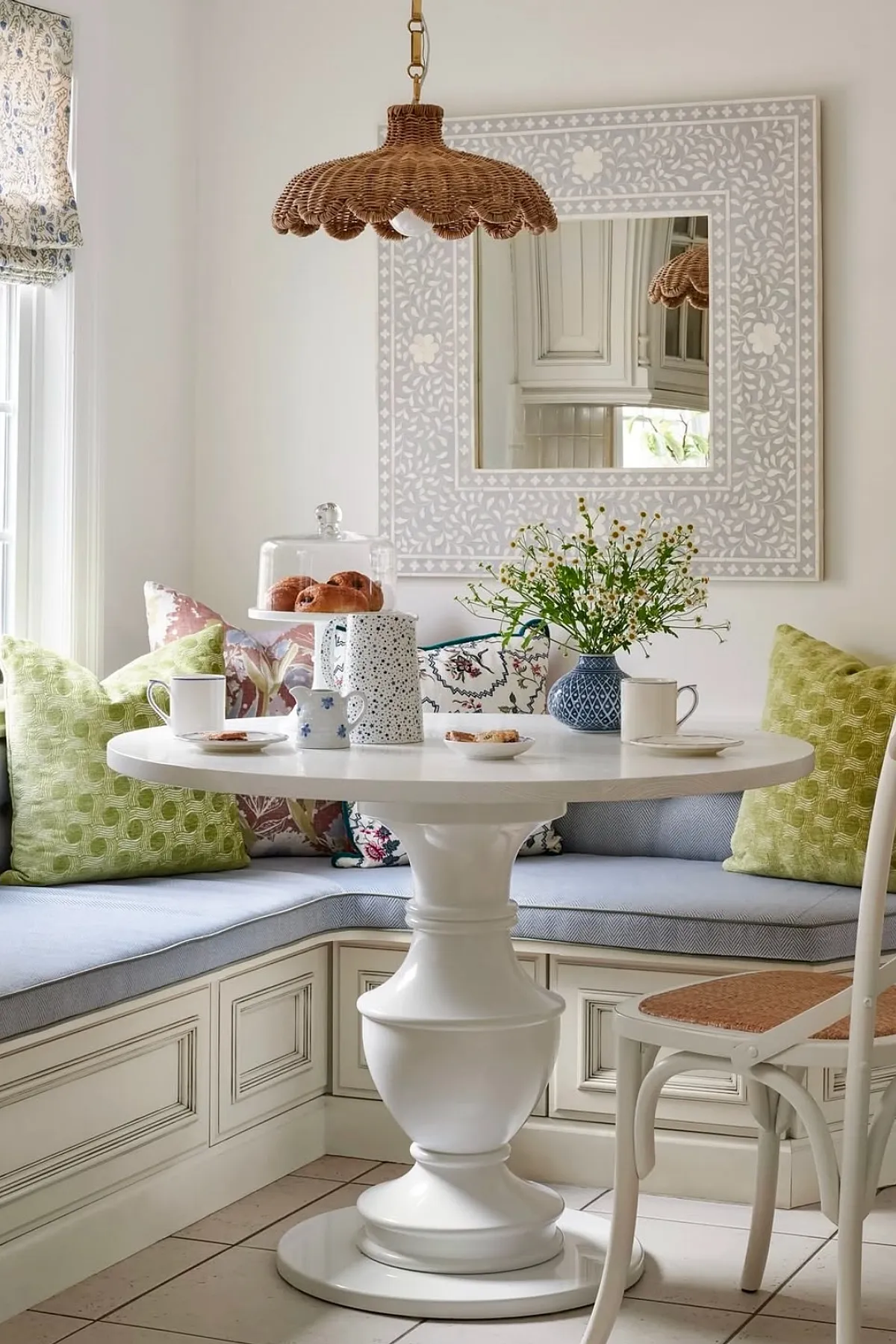 Charming breakfast nook featuring a white pedestal table, cozy bench seating with colorful cushions, and rattan light fixture.