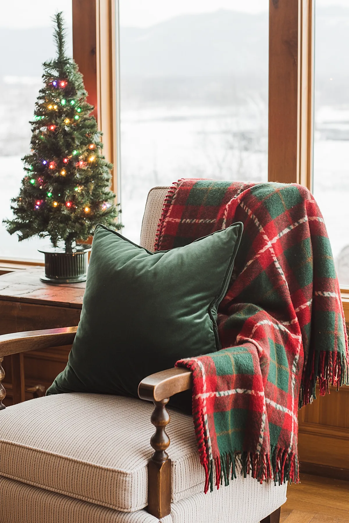 Armchair with red plaid throw, green velvet pillow, and a small lit tree nearby for a cozy corner that captures vintage christmas decor ideas.