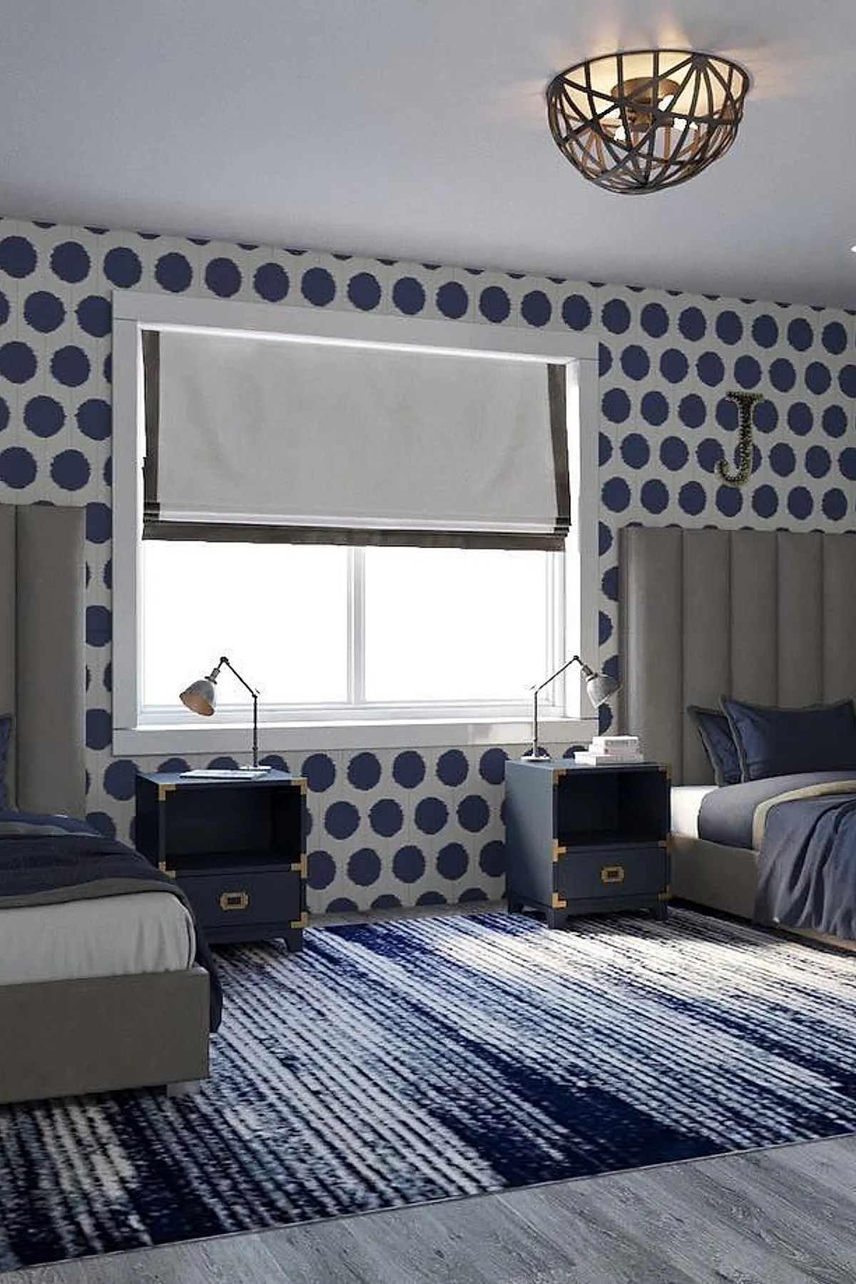 Bedroom with two twin beds featuring gray upholstered headboards, large navy blue polka dot wallpaper, matching navy bedside tables with gold corner accents, gray and navy bedding, white roman shades on window, and a blue patterned rug on gray wood flooring.