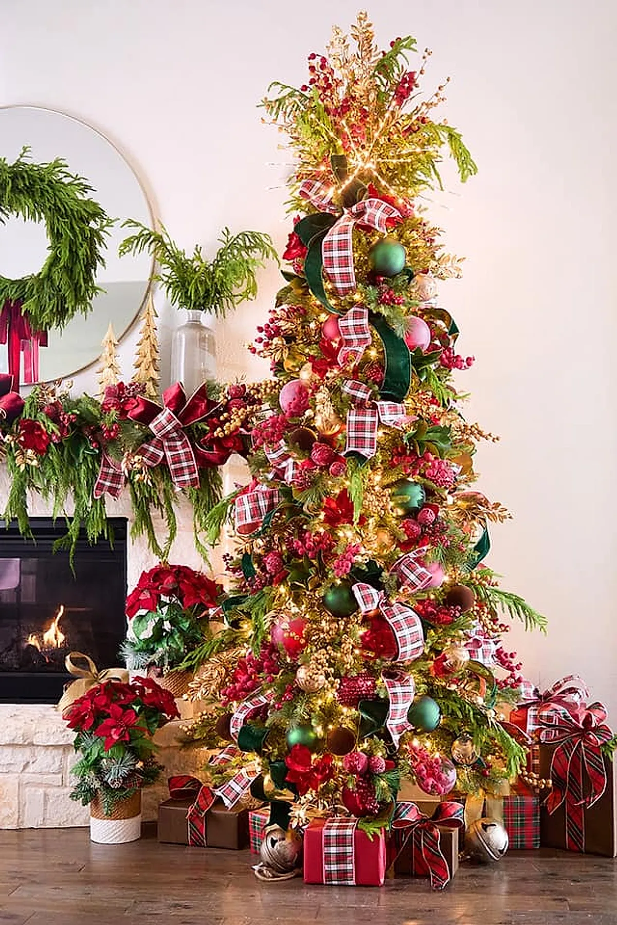 A Ralph Lauren Christmas tree decorated with traditional Christmas ornaments including red and green plaid ribbons, green velvet ribbons, red berries, gold leaves, and ornaments, surrounded by wrapped gifts in plaid and solid paper near a stone fireplace adorned with greenery and matching plaid bows.