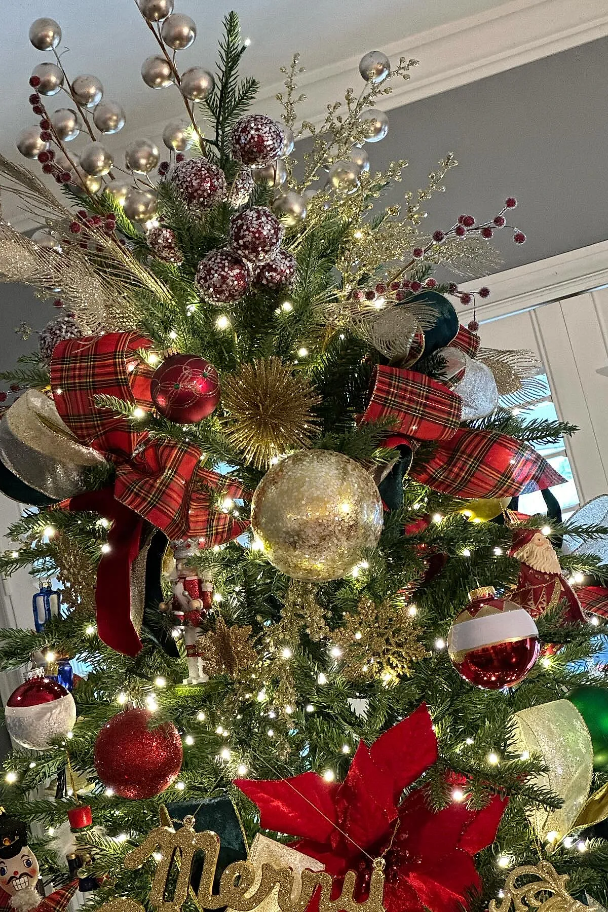 traditional christmas tree decorated with red plaid ribbon bows, gold glitter sprays, frosted berry clusters, and classic red, white, and gold round ornaments illuminated by warm white lights.