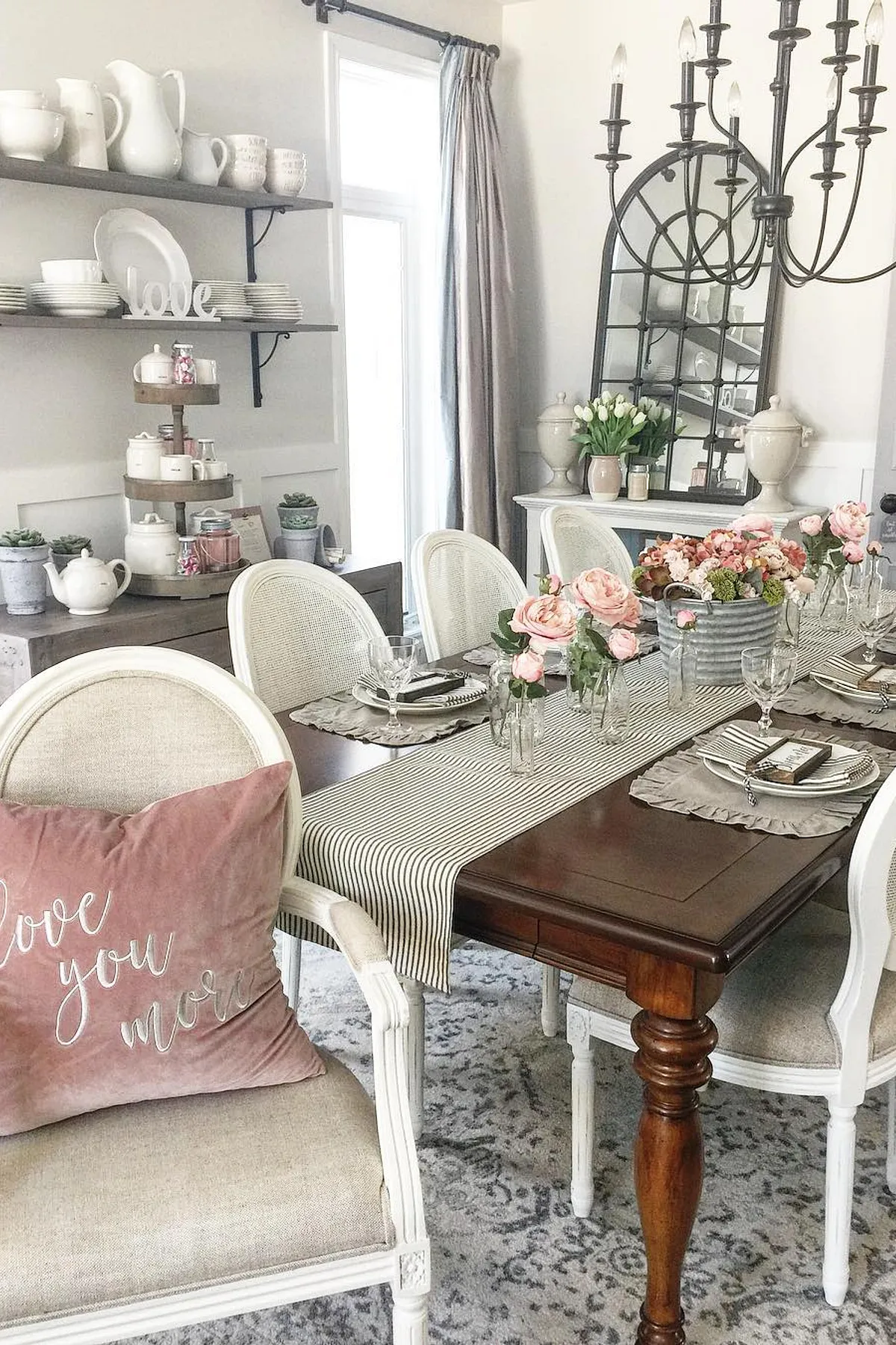 Cozy dining room with wooden table, striped runner, pink roses, chandelier, and