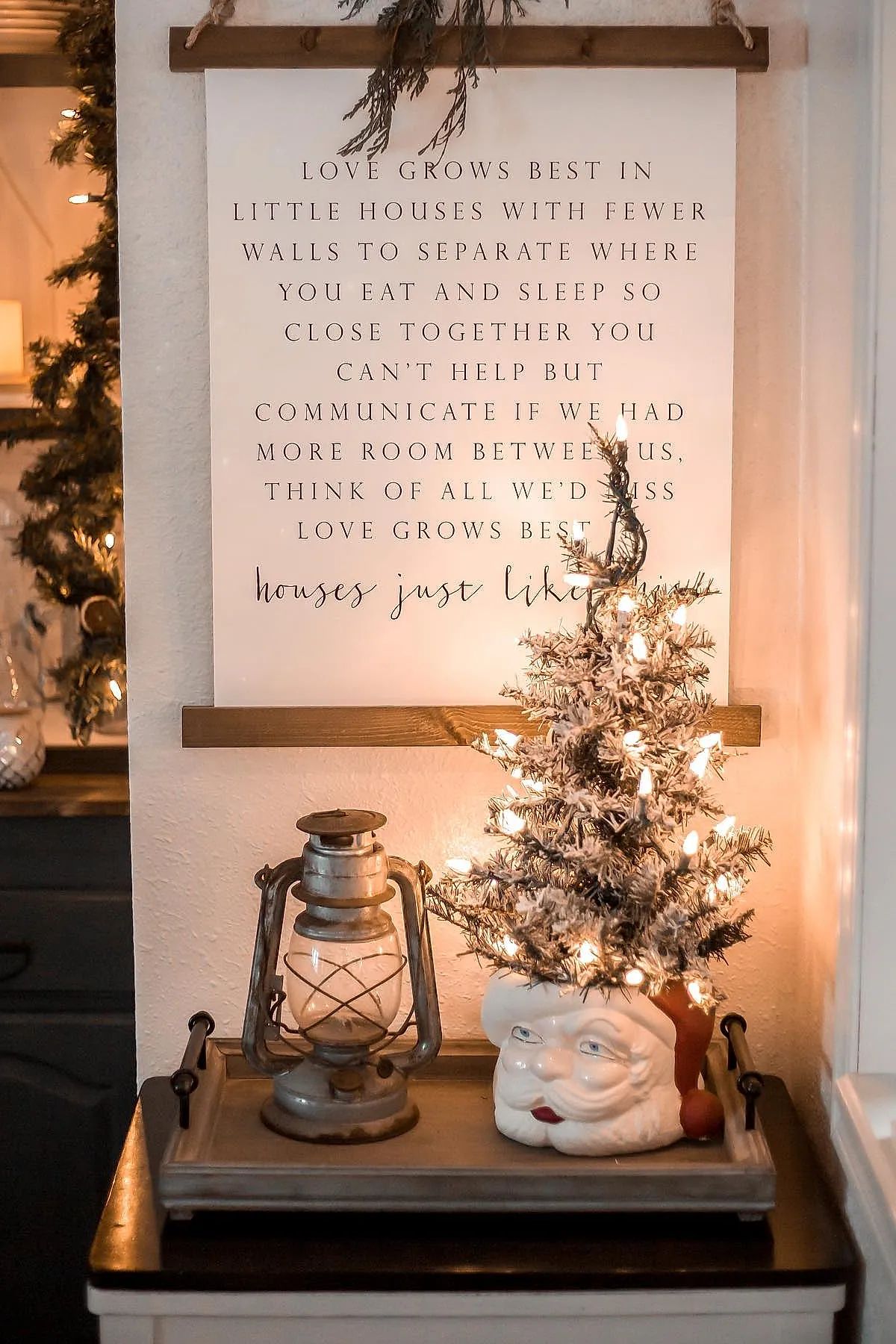 Mini christmas tree with frosted branches in a ceramic santa planter beside a metal lantern for a whimsical touch of vintage inspired christmas decor.
