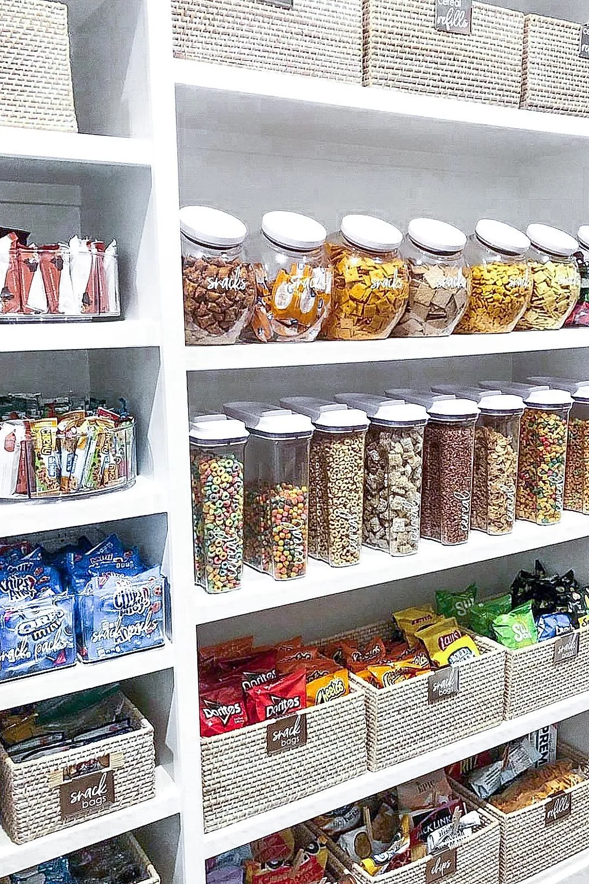 White pantry shelves neatly arranged with clear jars filled with various snacks and cereals, alongside woven baskets labeled