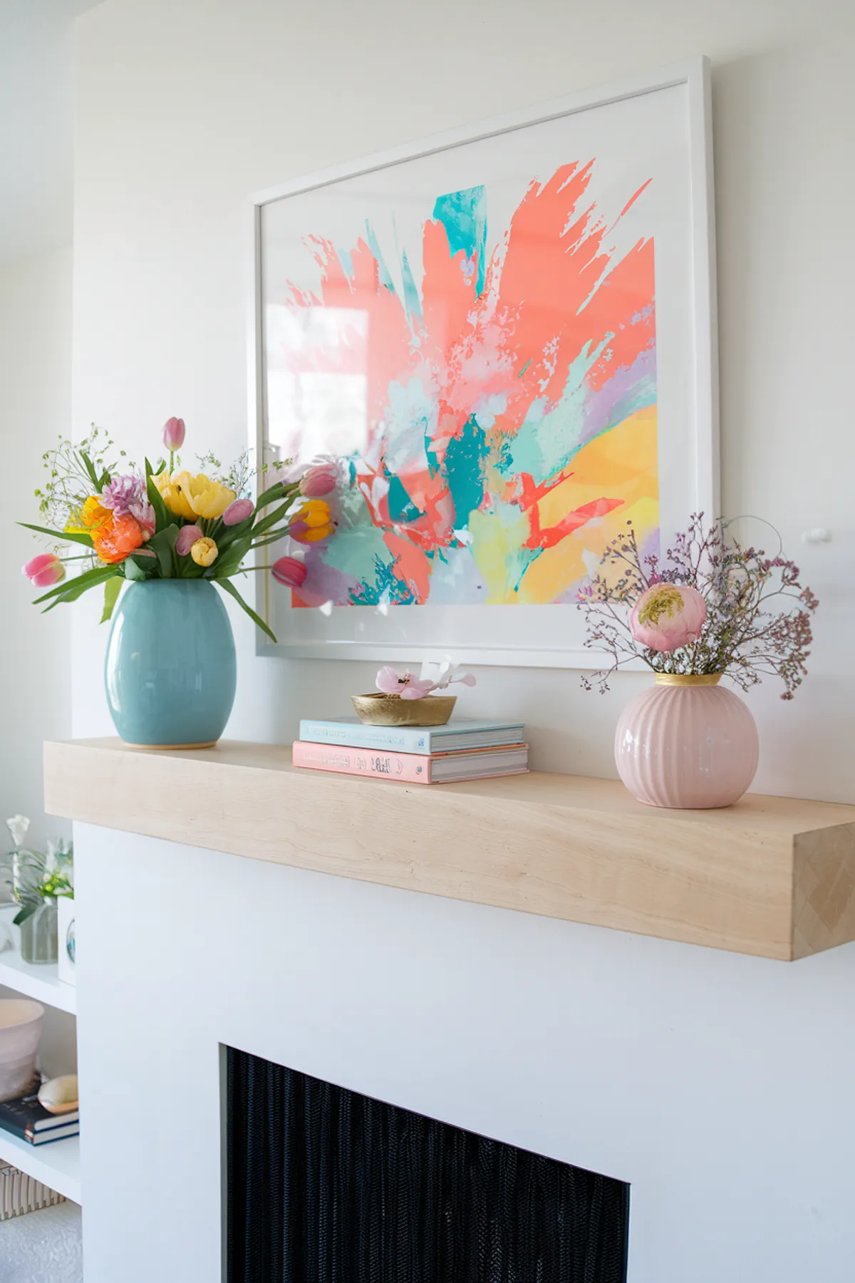 A colorful spring mantel featuring flowers, books, and vibrant wall art.