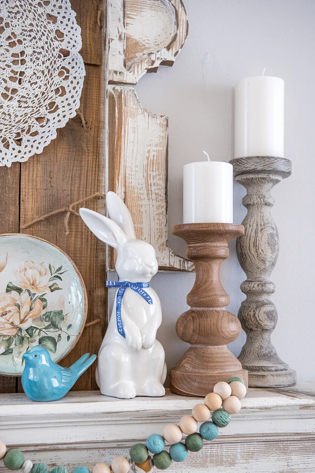 A whimsical spring mantel with a white bunny, blue bird, candles, and decorative beads.