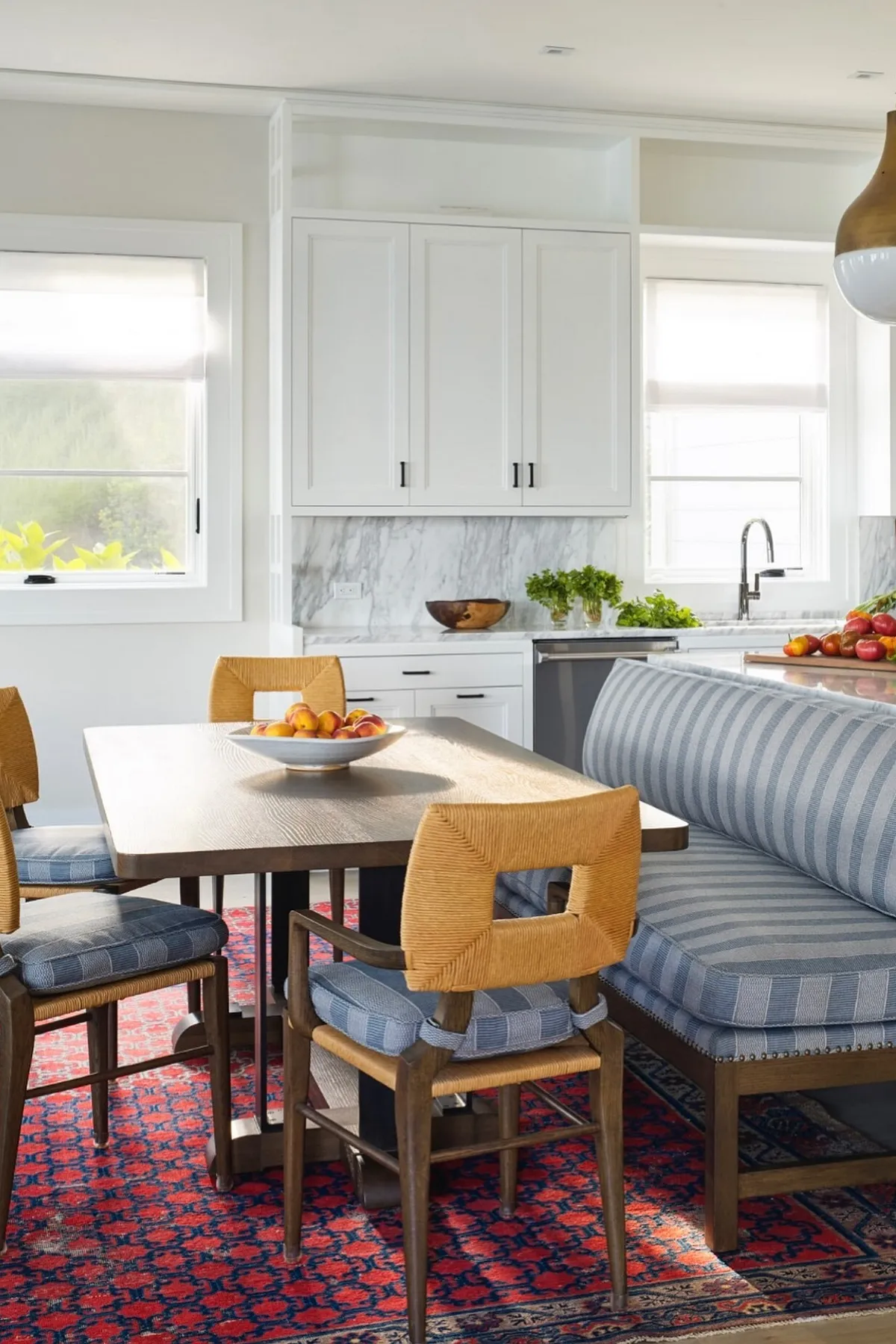Bright breakfast nook featuring a wooden table, striped bench seating, modern chairs, and colorful rug.