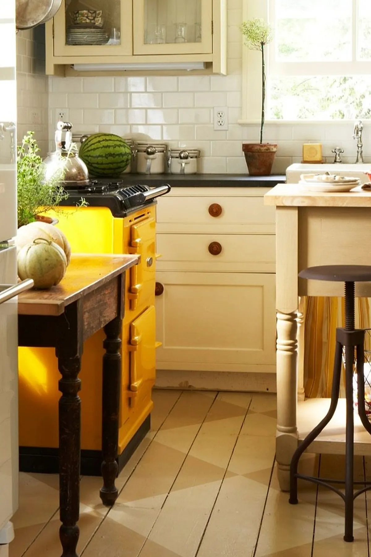 Vintage yellow kitchen stove in a small cottage kitchen with light yellow walls, wooden table, dark countertop, and cream-colored cabinets.