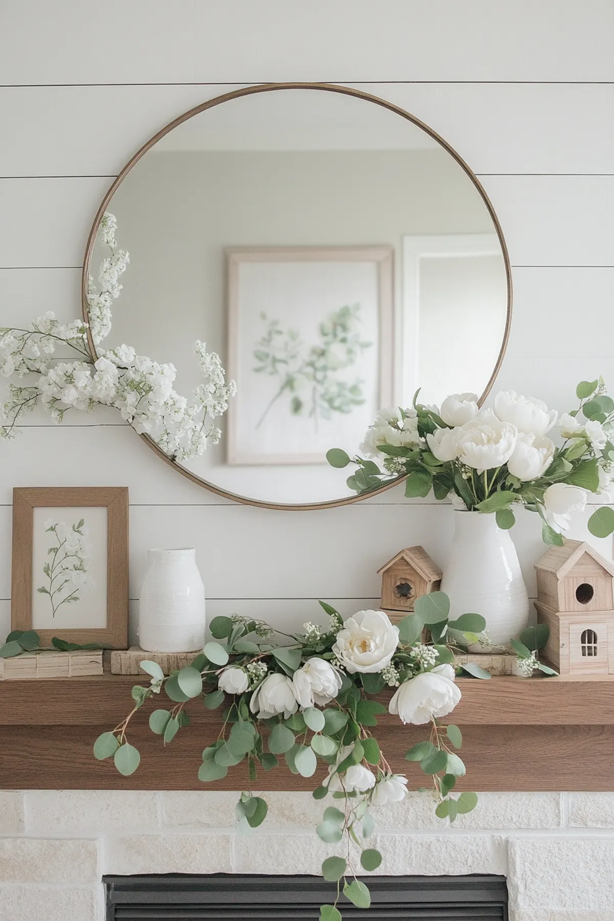 A spring mantel featuring white peonies, greenery, wooden houses, and a round mirror.
