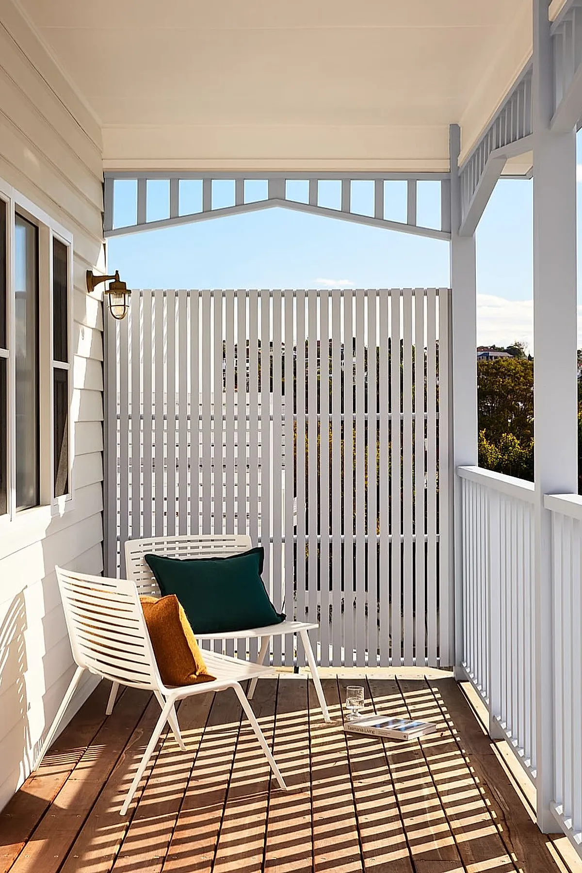 White vertical slatted privacy screen on a wooden patio with white chairs and colorful cushions.